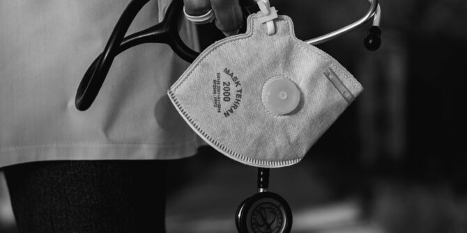 Hand with clear safety glove holding stethoscope and N95 mask