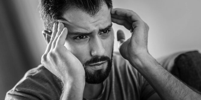 Man with goatee holding both temples with fingers