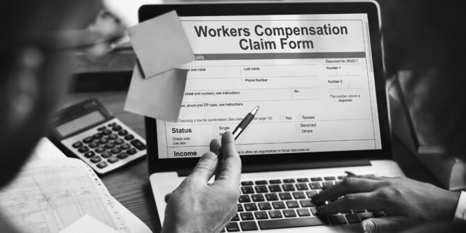 Two individuals filling out worker's compensation claim form on laptop