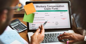 Two individuals filling out worker's compensation claim form on laptop