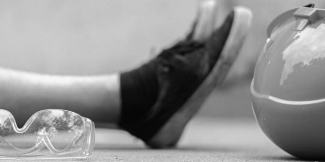 Eye safety glasses and orange construction helmet on ground in front of person's legs