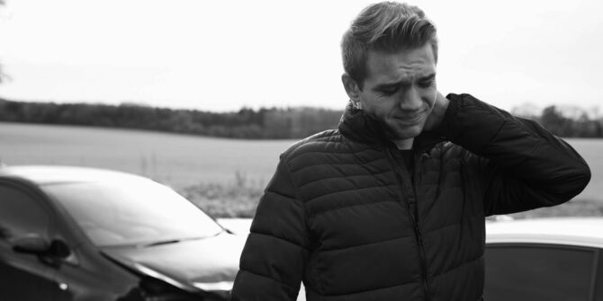 Man standing in front of car holding neck in discomfort