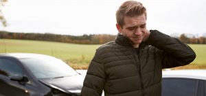 Man standing in front of car holding neck in discomfort