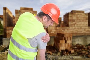 Leaning construction worker holding injured shoulder
