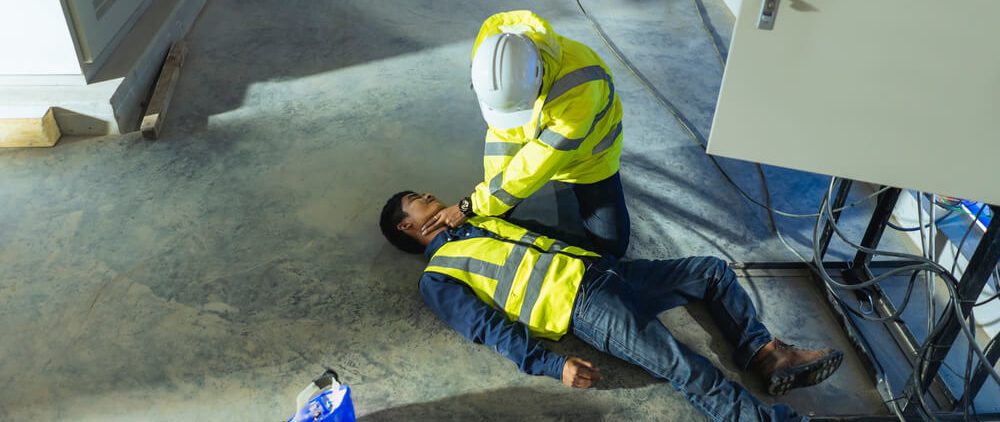 Construction worker checks the pulse of an unconcious coworker