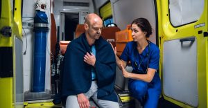 Man with emergency blanket draped over shoulders receiving care from EMT in ambulance