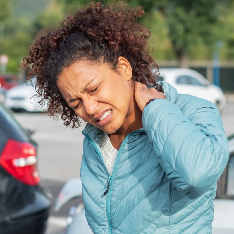 Woman in teal jacket clutching neck in pain