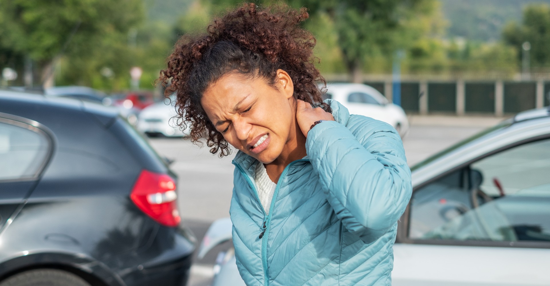 Woman in teal jacket clutching neck in pain