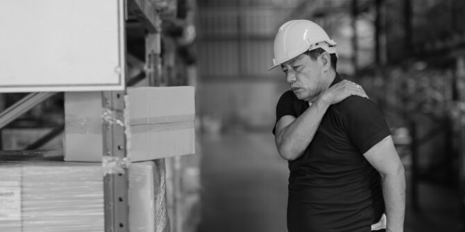 Male warehouse employee in blue shirt holding injured shoulder for workers comp