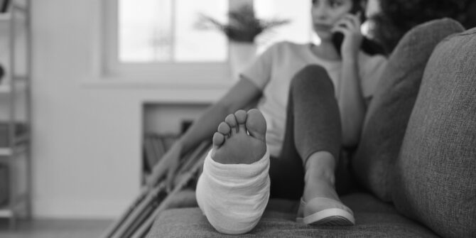 Woman talking on cell phone laying on couch with broken leg and crutches for worker's compensation blog post