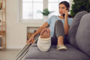 Woman talking on cell phone laying on couch with broken leg and crutches for worker's compensation blog post