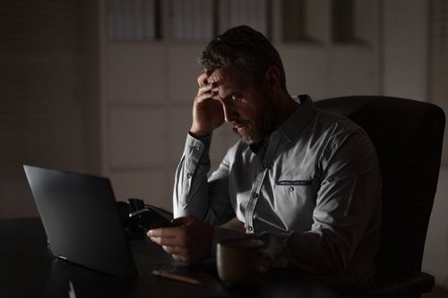 Tired businessman rubbing eyes while working at laptop late at office desk