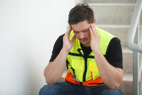 Tired construction worker in safety vest resting head on hand