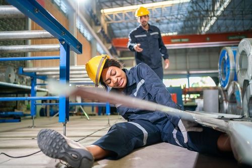 female factory worker in hard hat fallen on industrial floor after workplace accident