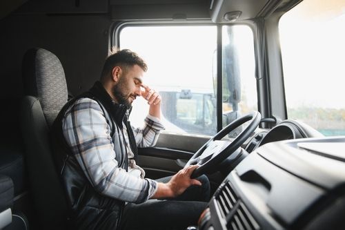fatigued truck driver gripping steering wheel with head bowed in cab